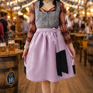 Op de afbeelding: Een dirndl-jurk met een grijs lijfje met ritssluiting aan de voorzijde, lange doorschijnende bordeauxrode mouwen met donker bloemenborduursel en een lichtpaarse satijnen rok met een zwart lint in de taille en zwarte rand onderaan.