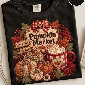 May include: A black t-shirt featuring a graphic of a quilted sign that reads Pumpkin Market, Hay Rides, and Corn Maze. The design includes pumpkins in various plaid patterns, a mug of whipped cream, red berries, and autumn leaves.