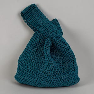 May include: A teal-coloured, handmade crochet bag. The bag has a knotted handle and a rounded, textured body. The crochet stitch creates a dense, durable fabric. The bag is designed for carrying items and has a simple, elegant design.