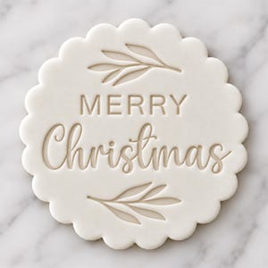 May include: A round white scalloped cookie stamp featuring the embossed text Merry Christmas in the center, flanked by a simple leaf sprig design above and below the lettering, creating a clean and clear holiday-themed impression.