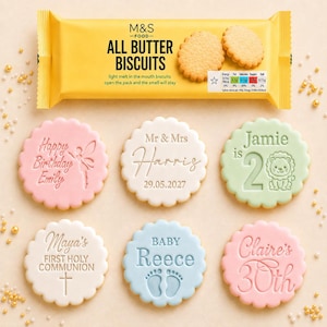 May include: A yellow M&S Food All Butter Biscuits packet positioned above six round scalloped biscuits featuring custom embossed designs including Happy Birthday Emily, Mr & Mrs Harris, Jamie is 2, Maya's First Holy Communion, Baby Reece, and Claire's 30th.