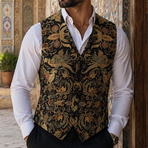 Puede incluir: Un chaleco sin mangas con base negra y un intrincado patrón floral y de volutas multicolor en tonos oro, bronce y azul apagado. El chaleco tiene cuello en V, cierre frontal con botones y se lleva sobre una camisa blanca impecable.
