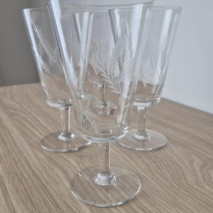 Può includere: Un set di quattro calici in vetro trasparente, ciascuno caratterizzato da un delicato motivo inciso raffigurante spighe di grano. I bicchieri presentano una coppa svasata, uno stelo sottile e una base circolare, per un design coerente.