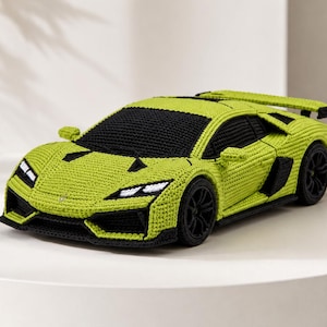 May include: A lime green and black crocheted sports car model featuring a low-profile aerodynamic body, a rear spoiler, black wheels, and detailed headlights. The textile construction mimics the sleek lines of a high-performance vehicle.