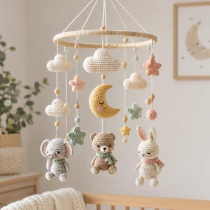 May include: A hanging nursery mobile featuring crocheted figures suspended from a circular wooden frame. The mobile includes a yellow crescent moon, a brown bear, a gray elephant, a white rabbit, various pastel-colored stars, and clouds.