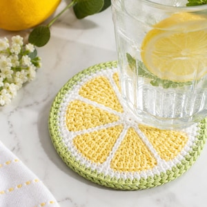 May include: A handmade crochet coaster shaped like a lemon slice. The coaster features yellow, white, and green yarn, with a glass of water and lemon on top. The coaster is approximately 4 inches in diameter.