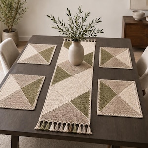 May include: A dining table set with a geometric pattern. The set includes a long table runner, four square placemats, and a vase with greenery. The runner and placemats feature a design of triangles in beige, olive green, and tan.