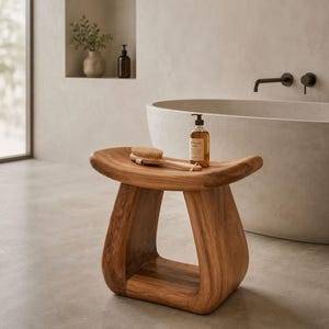 Puede incluir: Un taburete de madera curvada con un acabado de veta natural y suave. Sobre el asiento descansa un cepillo de baño de madera clara con una correa color canela y una botella de vidrio transparente con jabón líquido ámbar y dosificador negro.