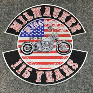 May include: A large embroidered patch featuring a motorcycle centred over an American flag background. The text MILWAUKEE WISCONSIN is arched above, with 1903-2018 in the centre, and 115 YEARS AMERICAN TRADITION arched below in red and white lettering.