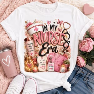 May include: A white t-shirt featuring a graphic print with the text "IN MY NURSE ERA". The design includes a nurse cap, a tumbler with "Fueled by coffee and Compassion", a mason jar, a notebook, a stethoscope, and a pink scrub top with a badge.