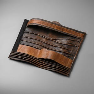 K&ouml;nnte beinhalten: Eine Werkzeugrolle aus braunem Leder mit mehreren horizontalen Taschen zur Aufbewahrung. Der Organizer hat eine dunkelbraune, strukturierte Oberfl&auml;che mit helleren, lohfarbenen Lederakzenten an den oberen und unteren Kanten zum Zusammenrollen.