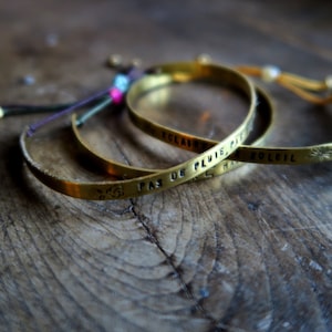 Puede incluir: Tres pulseras doradas con cordones ajustables. Las pulseras están grabadas con las frases francesas "Pas de pluie, pas de soleil", "Eclaircie" y "Harmonie".