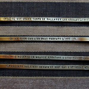 Pode incluir: Quatro barras de metal douradas com frases francesas inspiradoras gravadas nelas. As frases s&atilde;o: "Il est grand temps de rallumer les etoiles", "Le bien que l'on fait parfume l'ame", "J'accepte la grande aventure d'etre moi" e "Aujourd'hui, c'est demain et hier qui s'epousent".