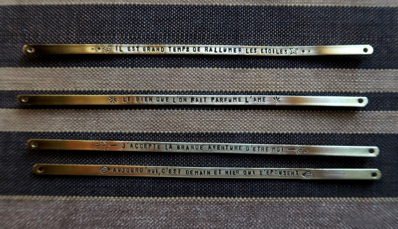 Pode incluir: Quatro barras de metal douradas com frases francesas inspiradoras gravadas nelas. As frases s&atilde;o: "Il est grand temps de rallumer les etoiles", "Le bien que l'on fait parfume l'ame", "J'accepte la grande aventure d'etre moi" e "Aujourd'hui, c'est demain et hier qui s'epousent".