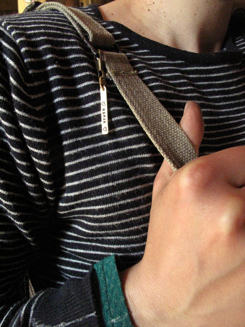 May include: A close-up of a person wearing a black and white striped shirt with a brown strap. The strap has a metal tag with the word "MAMAN" engraved on it.