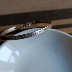 Pode incluir: Um bracelete de prata com a inscri&ccedil;&atilde;o "TOUS CEUX SINON ON VA DEVENIR DIEU".