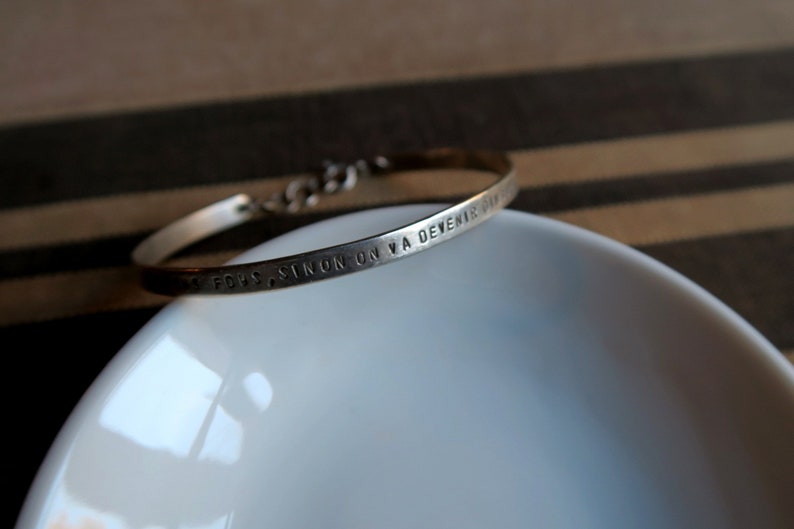 Pode incluir: Um bracelete de prata com a inscri&ccedil;&atilde;o "TOUS CEUX SINON ON VA DEVENIR DIEU".