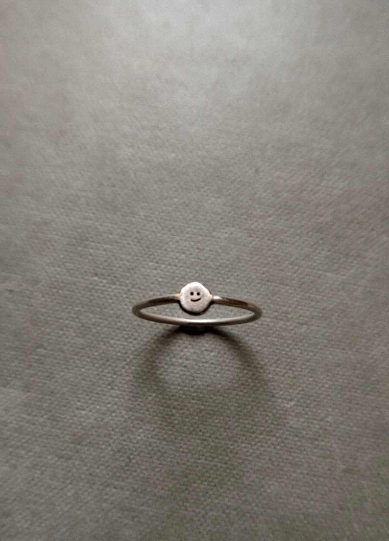 Pu&ograve; includere: Un anello d'argento con un piccolo design a forma di faccina sorridente.