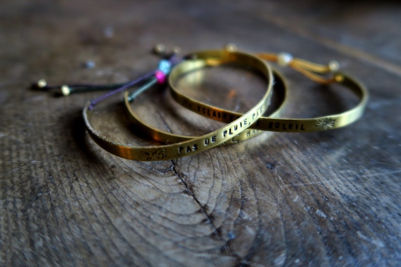 Pode incluir: Tr&ecirc;s pulseiras douradas com cord&otilde;es ajust&aacute;veis. As pulseiras s&atilde;o gravadas com as frases francesas "Pas de pluie, pas de soleil", "Eclaircie" e "Harmonie".