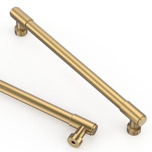 May include: Two T-bar cabinet pulls with a brushed brass finish. Each handle features a long, cylindrical bar attached to two cylindrical mounting posts. The design is sleek and metallic, showcasing a uniform gold-toned surface throughout the hardware.