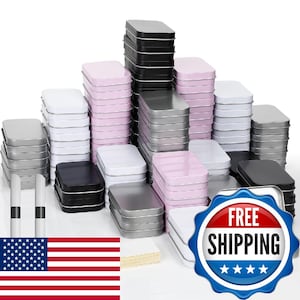 May include: A large collection of rectangular metal tins stacked in multiple columns. The tins feature a variety of solid colors including black, white, silver, and light pink. Each tin has a smooth finish and a removable lid.