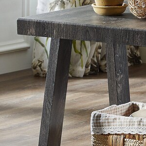 Puede incluir: Una mesa de madera gris oscuro con una textura de veta visible, que presenta una superficie rectangular y patas inclinadas resistentes. La superficie de la mesa es plana y lisa, mostrando un acabado desgastado que resalta el patrón natural.