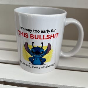 Peut inclure: Un mug en c&eacute;ramique blanche avec une illustration du personnage bleu Stitch de Lilo et Stitch. Le texte indique : It's way too early for THIS BULLSHIT. Sous le personnage, le texte ajoute : Me, to me, every single day. Le mug a une anse.