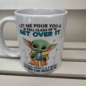 May include: White ceramic mug with a handle, featuring a green alien character illustration and the text "LET ME POUR YOU A TALL GLASS OF GET OVER IT OH AND HERE'S A STRAW SO YOU CAN SUCK IT UP".