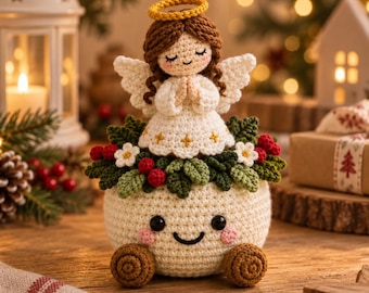 Puede incluir: Una figura de ángel tejida a ganchillo con cabello castaño y halo amarillo, vistiendo un vestido blanco, colocada sobre una base redonda de color crema con una cara sonriente, decorada con hojas verdes, flores blancas y bayas rojas.