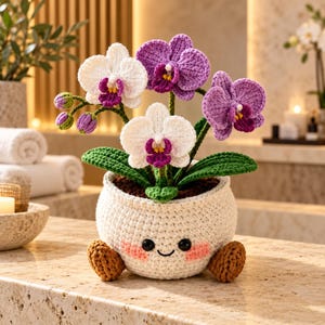 May include: A crocheted orchid plant with white and purple flowers, green leaves, and brown buds, potted in a round white crocheted container featuring a smiling face with black eyes, a small mouth, and pink cheeks, supported by two brown feet.