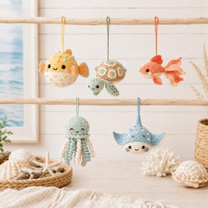 May include: Five hanging crochet ornaments featuring sea creatures: a yellow pufferfish, a green and brown turtle, an orange goldfish, a light green jellyfish with dangling tentacles, and a blue spotted stingray, all suspended from wooden rods.