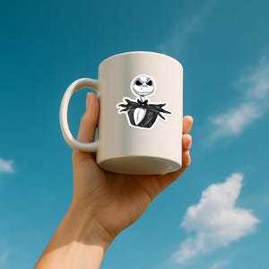 May include: A white ceramic mug featuring a black and white graphic illustration of a skeletal character with a wide grin, wearing a pinstriped suit and a bat-shaped bowtie. The mug has a smooth finish and a curved handle on the left side.
