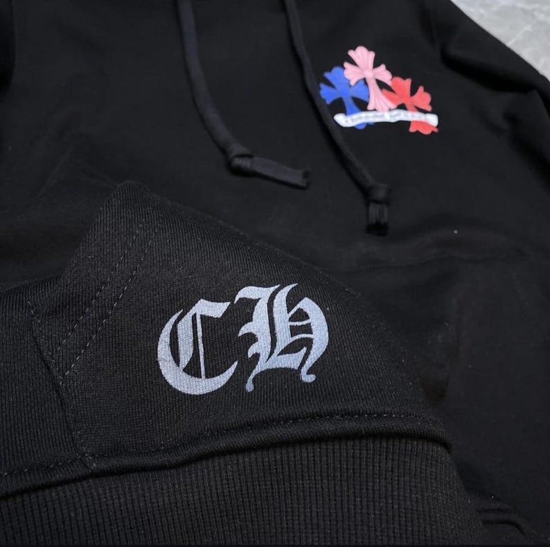May include: Black hoodie with a drawstring hood and a front pocket. Features a colorful cross design on the upper chest and a "CH" logo on the sleeve cuff. The cross design includes pink, blue, and red colors.