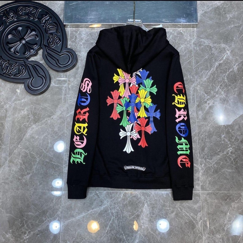 May include: Black hoodie with a colorful cross design. The sleeves feature the text "CHROME HEARTS" in rainbow colors. The hoodie has a drawstring hood and a front pocket.