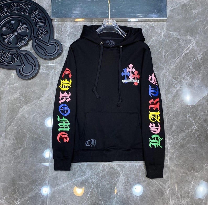 May include: Black hooded sweatshirt with colorful "CHROME" lettering down the left sleeve and "HEARTS" down the right sleeve. A small logo is on the chest and a larger logo with crosses is on the chest. The sweatshirt has a front pocket.