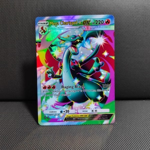 Op de afbeelding: Een holografische Mega Charizard X EX ruilkaart met een zwart, draakachtig wezen met blauwe vlammen, rode vleugels en een regenboogkleurige achtergrond. De kaart toont 220 HP, de Raging Blaze aanval en diverse spelstatistieken.