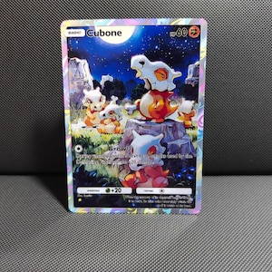 May include: A holographic Cubone trading card featuring a night scene with multiple Cubone characters in a grassy field under a full moon. The card displays the name Cubone, 60 HP, the Growl attack text, and a fighting type symbol in the top corner.