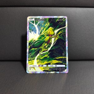 Pode incluir: Um cartão colecionável holográfico com um personagem Treecko verde em um cenário de floresta. O cartão tem a palavra "Basic" no topo, com o nome "Treecko" acima do personagem. O cartão também tem a palavra "Pound" e o número "20".