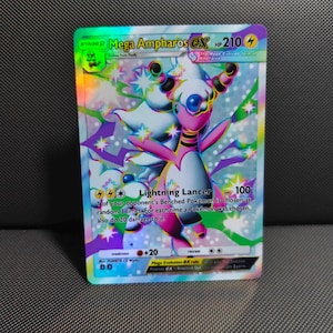 May include: A holographic Mega Ampharos EX trading card featuring a pink and white creature with long ears and a blue orb on its forehead. The card displays the text Mega Ampharos EX, HP 210, and Lightning Lancer 100, set against a vibrant rainbow background.
