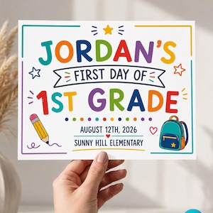 May include: A rectangular white sign with colorful text reading Jordan's First Day of 1st Grade, August 12th, 2026, and Sunny Hill Elementary. The design features a yellow pencil, a blue backpack, stars, and a border in a multi-colored line style.