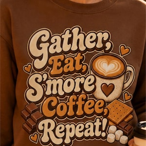Może przedstawiać: Brązowa bluza z okrągłym dekoltem z nadrukiem graficznym zawierającym tekst "Gather, Eat, S'more Coffee, Repeat!" w stylu retro. Wzór przedstawia kubek kawy z latte art w kształcie serca, kawałki czekolady, herbatniki oraz pianki marshmallow.