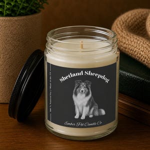 Peut inclure: Une bougie en pot de verre avec un couvercle noir. L'étiquette présente une illustration de Shetland Sheepdog sur fond noir. Le texte sur l'étiquette indique "Shetland Sheepdog" et "Ember Pet Candle Co."