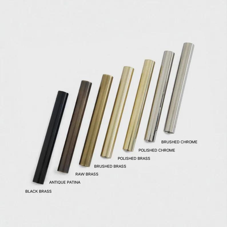 K&ouml;nnte beinhalten: Sieben zylindrische Schrankgriffe aus Metall, diagonal angeordnet und beschriftet als Black Brass, Antique Patina, Raw Brass, Brushed Brass, Polished Brass, Polished Chrome und Brushed Chrome, die eine Vielzahl von Metalloberfl&auml;chen zeigen.