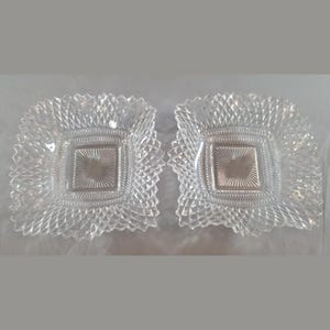 Puede incluir: Dos platos cuadrados de cristal transparente con un patrón de diamantes prensados en la superficie y una sección central cuadrada con líneas radiantes. Los bordes de los platos son festoneados y tienen textura.