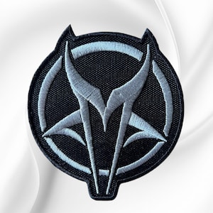 May include: A circular embroidered patch featuring a black background with a stylized, light gray wolf head silhouette integrated into a circular frame. The design uses dense stitching to create sharp, angular lines and a distinct, symmetrical emblem.