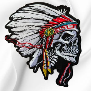May include: An embroidered patch featuring a skull wearing a large white feathered headdress. The headdress includes red, turquoise, and yellow accents with a geometric pattern. The skull is depicted in white and grey thread on a black background.