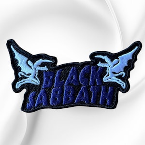 May include: An embroidered patch featuring the text BLACK SABBATH in dark blue thread on a black background. The design is flanked by two light blue winged figures, one on each side, with a dark blue border outlining the entire shape of the patch.