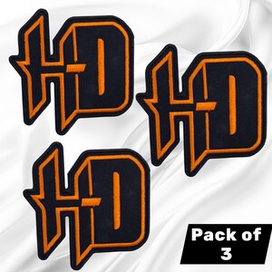 May include: A set of three embroidered patches featuring the letters HD in a stylized font. Each patch has a black center with a bold orange border. The text Pack of 3 is displayed in white on a black rectangular background in the corner.