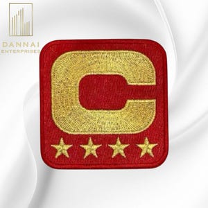 May include: A red embroidered patch with a gold letter "C" and four gold stars. The patch is square with rounded corners. The logo for Dannai Enterprises is in the upper left corner.