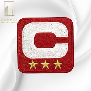 May include: A red embroidered patch with a white "C" design and three gold stars at the bottom. The patch is square with rounded corners. The text "DANNAI ENTERPRISES" is in the upper left corner.